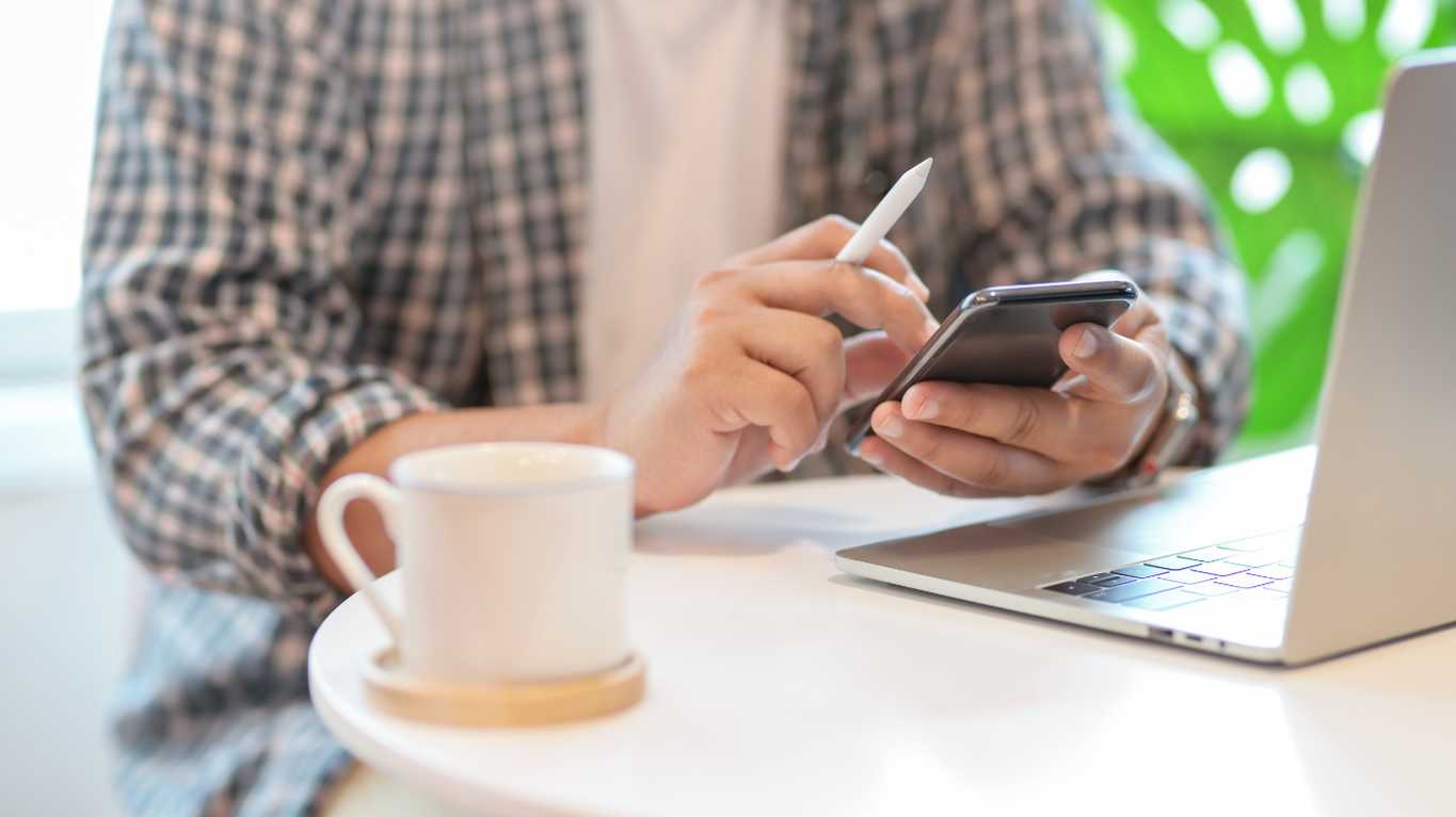 Person sitting with laptop cell phone and cup of coffee getting ready to contact us Person sitting with laptop cell phone and cup of coffee getting ready to contact us